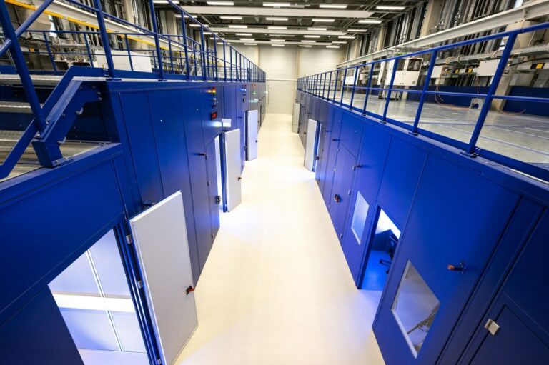 In den Kammern der Versuchshalle sind die Prüfstände einzeln eingehaust - zum Schallschutz und aus Sicherheitsgründen. Während der Versuche bleiben die Türen verschlossen, da in den Prüfständen mit Schadgasen gearbeitet wird. Im oberen Hallenbereich ist die technische Infrastruktur sichtbar, wie etwa Leitungen für die Schadgase, Kühlwasser und die Laserquellen. Credit: DLR (CC BY-NC-ND 3.0)